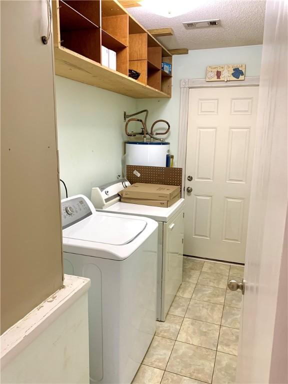 laundry room featuring visible vents, a textured ceiling, washing machine and dryer, gas water heater, and light tile patterned floors