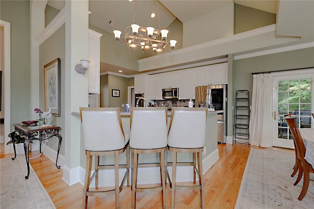 kitchen featuring stainless steel appliances, crown molding, a peninsula, white cabinetry, and a chandelier