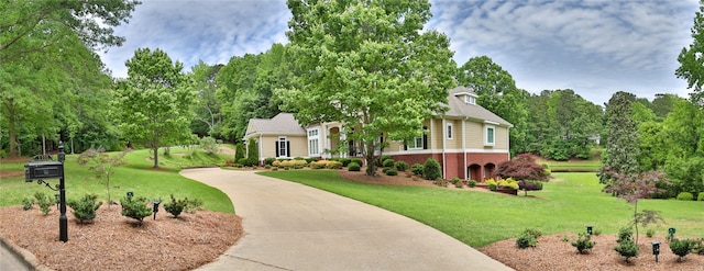 view of front of property featuring concrete driveway, a front yard, brick siding, and view of scattered trees