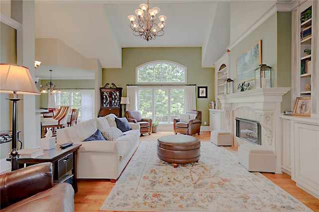 living room featuring a chandelier, light wood-style flooring, high vaulted ceiling, and a glass covered fireplace