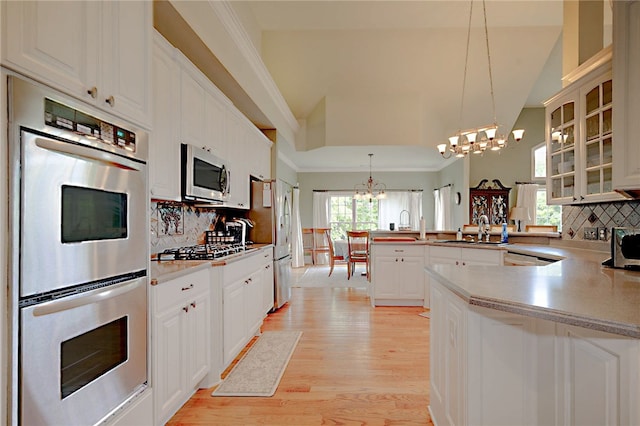 kitchen with a chandelier, a peninsula, appliances with stainless steel finishes, glass insert cabinets, and tasteful backsplash