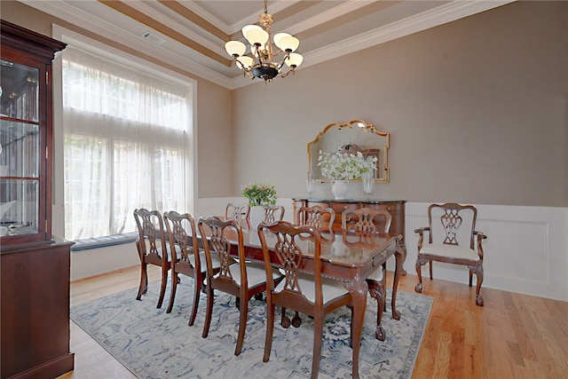 dining room with ornamental molding, a chandelier, light wood-style flooring, and a wainscoted wall