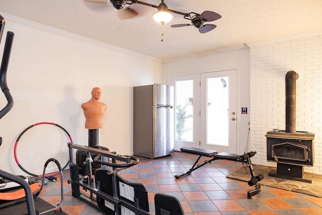 workout room featuring ceiling fan, ornamental molding, and a wood stove