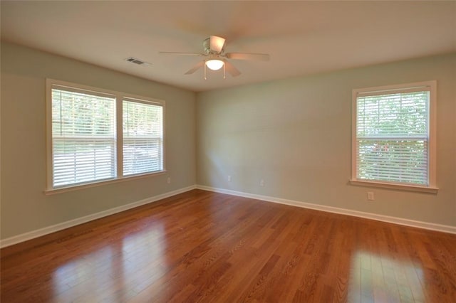 empty room with wood finished floors, ceiling fan, visible vents, and plenty of natural light