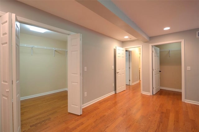 unfurnished bedroom featuring a closet, recessed lighting, a walk in closet, light wood finished floors, and baseboards