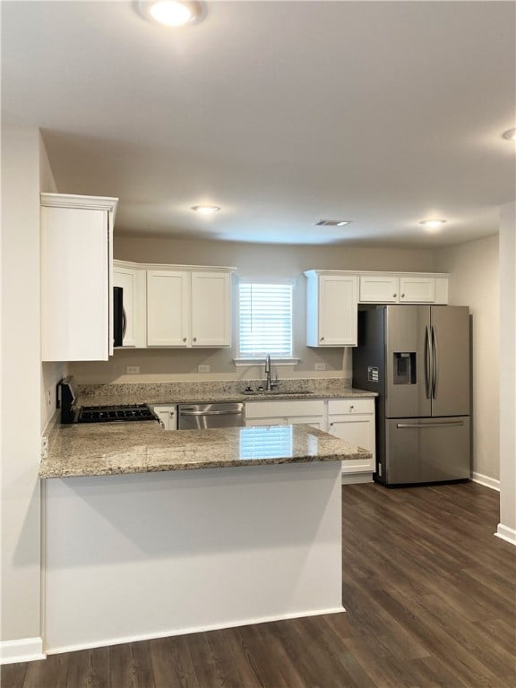 kitchen featuring dark wood finished floors, appliances with stainless steel finishes, light stone counters, a peninsula, and a sink