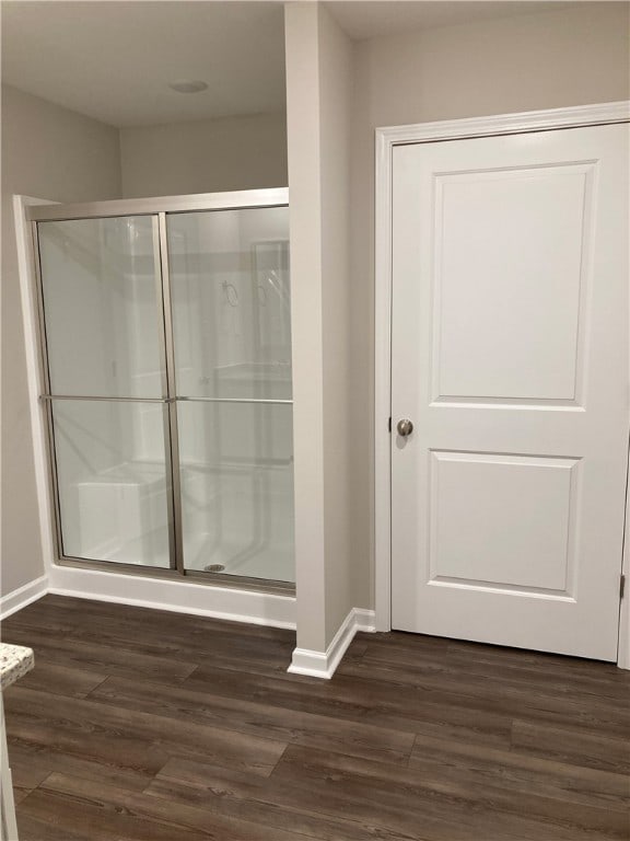 full bathroom with wood finished floors, a shower stall, and baseboards