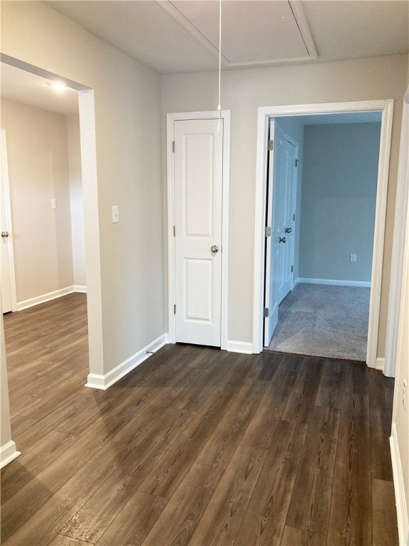 empty room with attic access, baseboards, and dark wood-type flooring