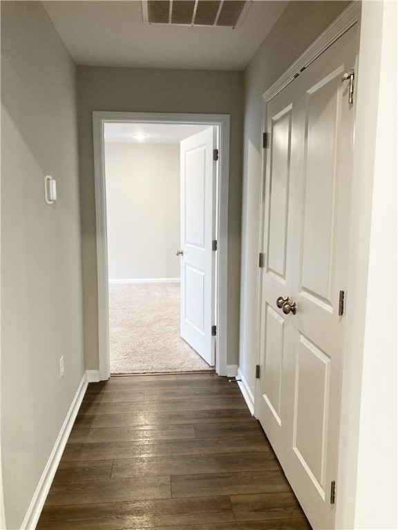 corridor with baseboards, visible vents, and dark wood finished floors