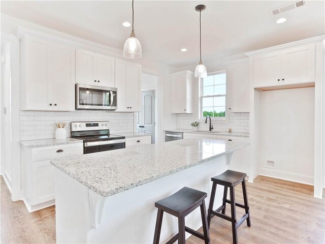 8 Crossing Ct E, Valley, AL 36854 - kitchen featuring stainless steel appliances, white cabinets, a center island, light wood-style floors, and backsplash
