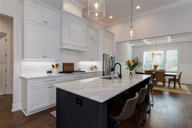 kitchen with appliances with stainless steel finishes, white cabinetry, hanging light fixtures, and a kitchen island with sink