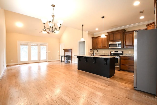 kitchen with light hardwood / wood-style flooring, a breakfast bar area, hanging light fixtures, stainless steel appliances, and a center island with sink