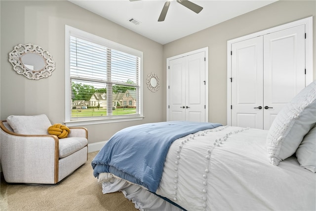 bedroom featuring a ceiling fan, visible vents, carpet floors, baseboards, and two closets