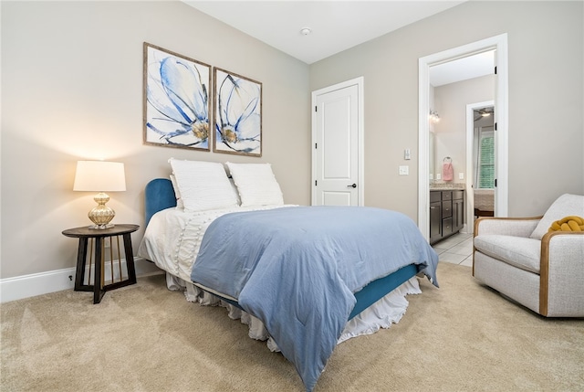 bedroom featuring baseboards, ensuite bathroom, and light colored carpet