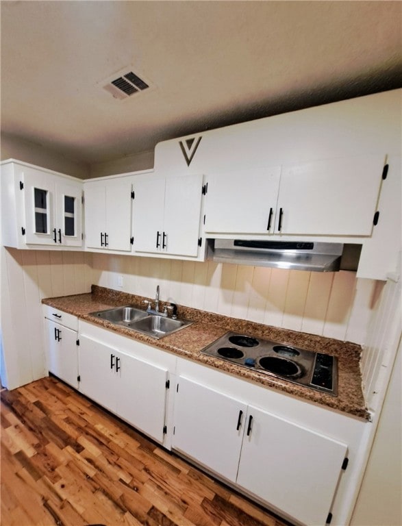 kitchen with stovetop, sink, dark stone countertops, light hardwood / wood-style floors, and white cabinets