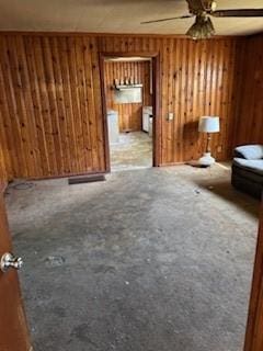unfurnished living room featuring ceiling fan and wooden walls