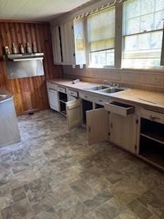 kitchen featuring stone finish floor, exhaust hood, wood walls, a sink, and light countertops