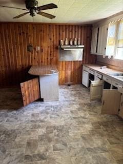 kitchen featuring wooden walls, stone finish floor, ceiling fan, and light countertops