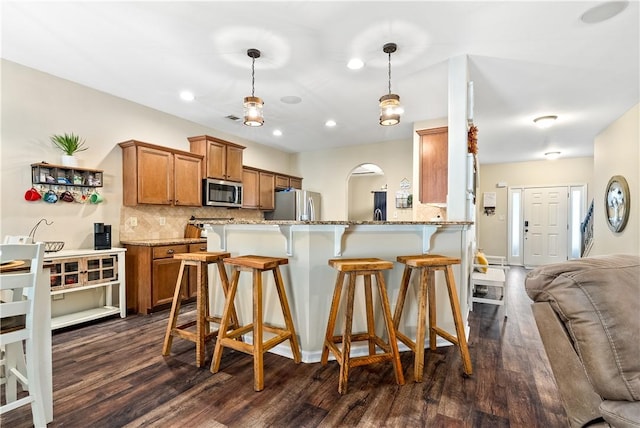 172 Solamere Ln, Auburn, AL 36832 - kitchen featuring appliances with stainless steel finishes, brown cabinets, dark wood-style floors, a kitchen breakfast bar, and light stone countertops