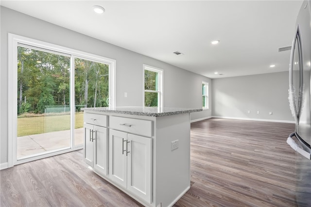 kitchen with light stone countertops, a center island, light hardwood / wood-style flooring, stainless steel fridge, and white cabinets