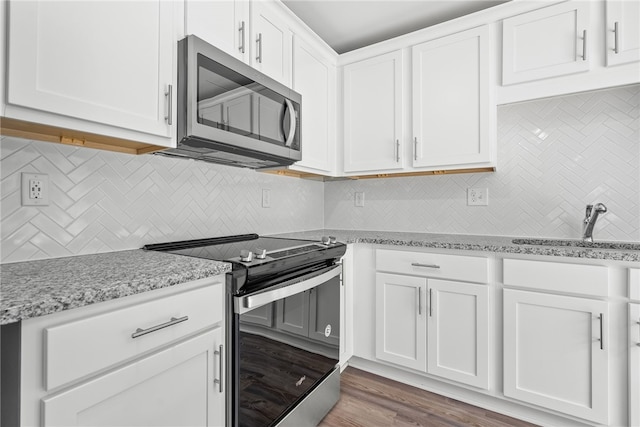 kitchen with backsplash, white cabinets, hardwood / wood-style flooring, appliances with stainless steel finishes, and light stone counters