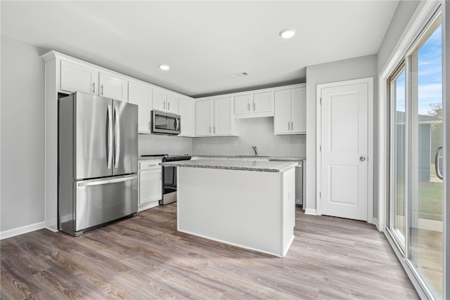 kitchen featuring a kitchen island, appliances with stainless steel finishes, light hardwood / wood-style floors, light stone counters, and white cabinetry