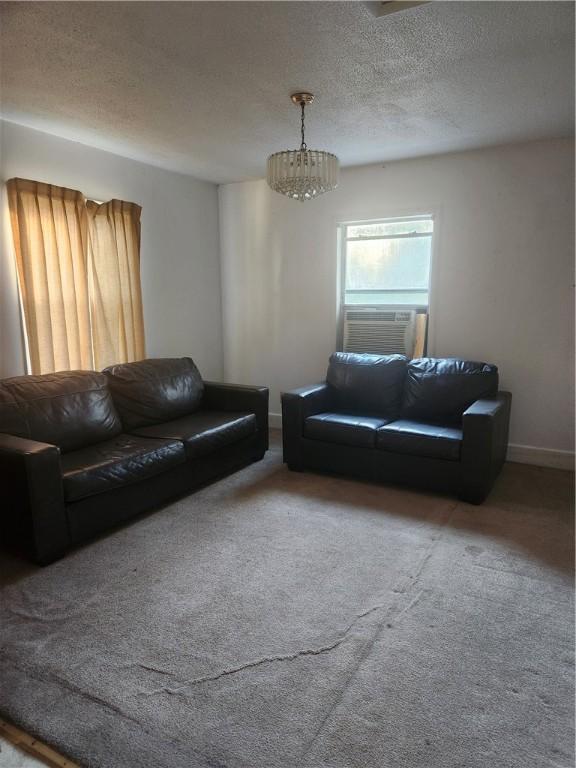 living room featuring cooling unit, carpet floors, a textured ceiling, and a notable chandelier