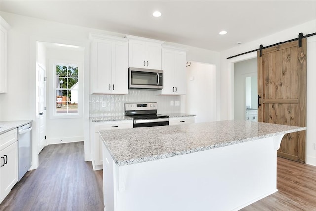 112 Hunters Way, Opelika, AL 36801 - kitchen with appliances with stainless steel finishes, wood finished floors, a barn door, white cabinetry, and light stone counters