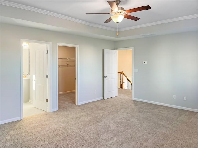 unfurnished bedroom featuring light carpet, ensuite bathroom, ceiling fan, a spacious closet, and ornamental molding