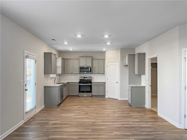 kitchen featuring decorative backsplash, appliances with stainless steel finishes, light wood-type flooring, and gray cabinets