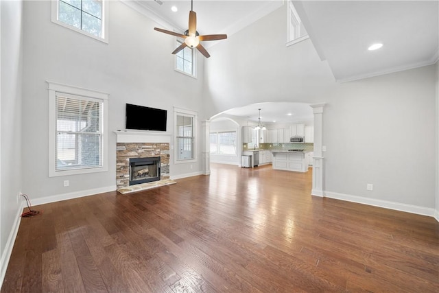 unfurnished living room with crown molding, a stone fireplace, dark wood-type flooring, and ceiling fan