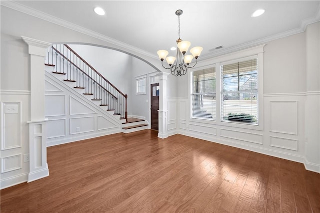 unfurnished dining area with crown molding, a chandelier, hardwood / wood-style floors, and ornate columns