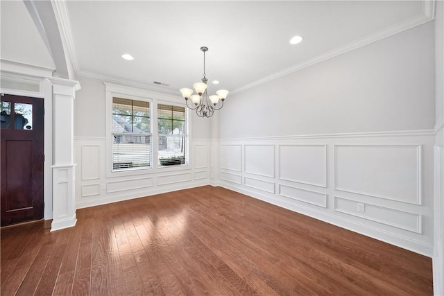 unfurnished dining area featuring crown molding, decorative columns, dark hardwood / wood-style floors, and a chandelier