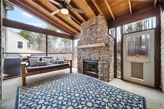 sunroom / solarium featuring vaulted ceiling with beams, wooden ceiling, an outdoor stone fireplace, and ceiling fan