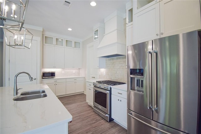 kitchen with sink, decorative light fixtures, high quality appliances, light stone countertops, and white cabinets