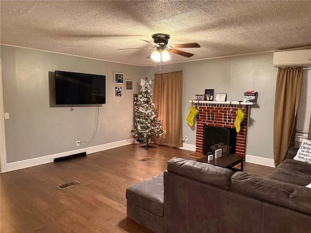 living room featuring a textured ceiling, a wall mounted AC, ceiling fan, wood-type flooring, and a fireplace