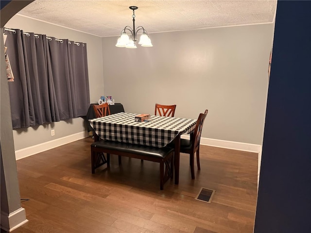 dining space with dark wood-type flooring, a textured ceiling, and an inviting chandelier