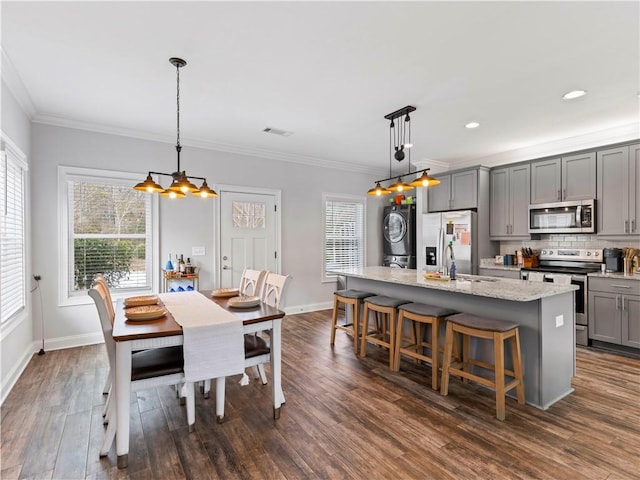 kitchen featuring pendant lighting, an island with sink, gray cabinetry, stainless steel appliances, and dark wood-type flooring