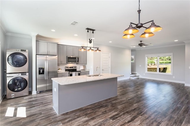 kitchen with gray cabinetry, hanging light fixtures, stainless steel appliances, stacked washer / dryer, and an island with sink