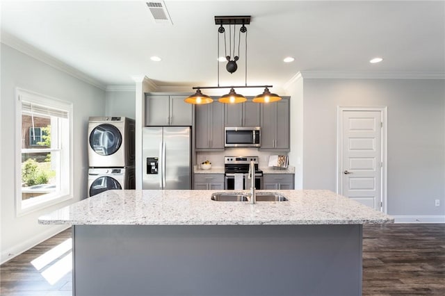 kitchen with gray cabinetry, hanging light fixtures, stainless steel appliances, stacked washer / dryer, and an island with sink