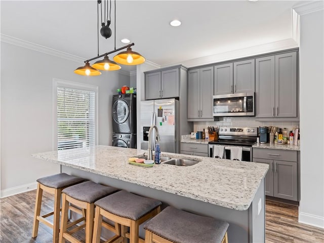 kitchen featuring stacked washer and dryer, sink, a center island with sink, appliances with stainless steel finishes, and pendant lighting