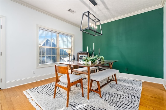 dining area with wood-type flooring, ornamental molding, and an inviting chandelier