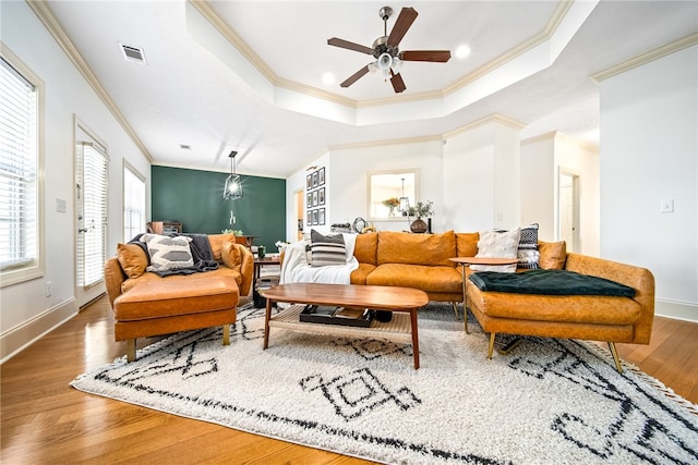 living room with a raised ceiling, ceiling fan, plenty of natural light, and wood-type flooring