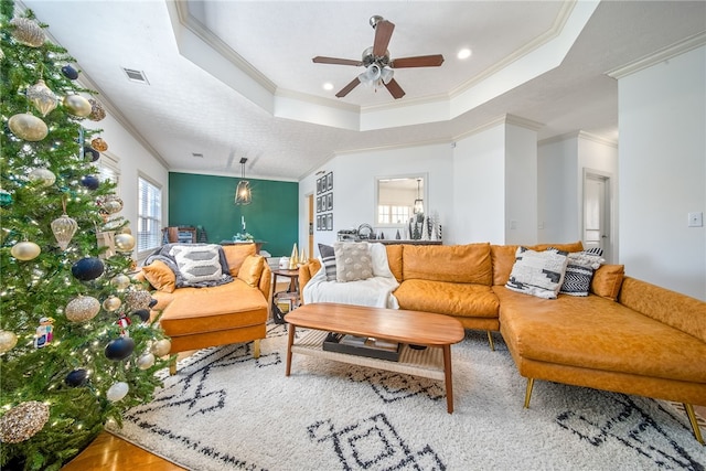 living room featuring ceiling fan, ornamental molding, and a raised ceiling