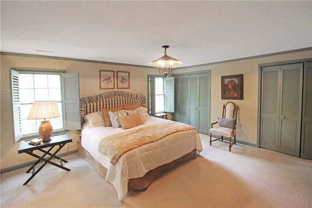 bedroom with light carpet, ornamental molding, and multiple closets