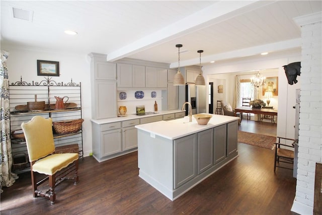 kitchen with gray cabinetry, stainless steel refrigerator with ice dispenser, an island with sink, beamed ceiling, and decorative light fixtures