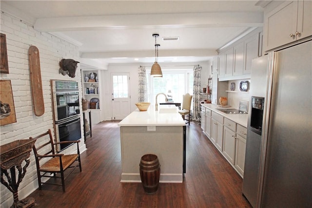 kitchen with beam ceiling, dark wood-type flooring, stainless steel fridge, an island with sink, and decorative light fixtures