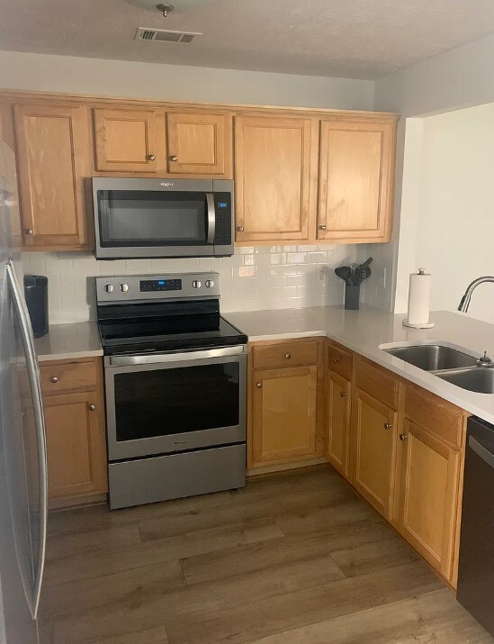 kitchen with tasteful backsplash, light countertops, appliances with stainless steel finishes, wood finished floors, and a sink