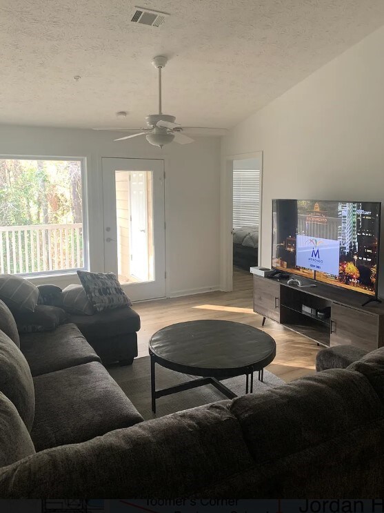 living room featuring visible vents, a textured ceiling, light wood-style flooring, and vaulted ceiling