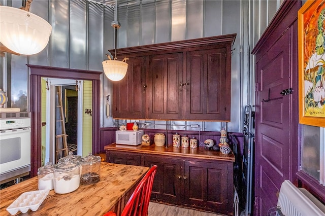 kitchen featuring light wood-style flooring, a decorative wall, white appliances, wooden counters, and dark brown cabinets